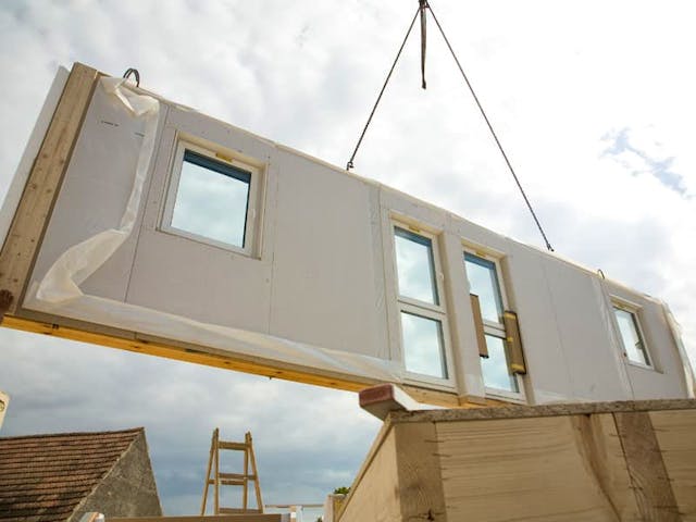 Ein Kran lädt eine in der Fabrik gefertigte Rohbauwand ab. Auf der Baustelle wird aus den Wänden ein Haus zusammengesetzt. Foto: benik.at / stock.adobe.com