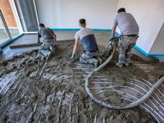 Estrich, Bild eines Raumes, in dem von drei Bauarbeitern Estrich über einer Fußbodenheizung verlegt wird, Foto: Wolfilser / stock.adobe.com