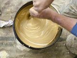 Farbe und Lack, Bild eines Mannes, der einen Farbeimer vor sich hat und die darin befindliche beige Farbe mit weiß abtönt und umrührt, Foto: iStock.com / MPKphoto