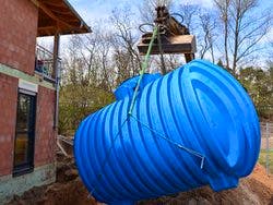Zisterne, Bild eines blauen Wassertanks der mittels eines kleinen Krans in eine Baugrube gehoben wird neben einem im Bau befindenden Haus, Foto: Ilhan Balta / stock.adobe.com
