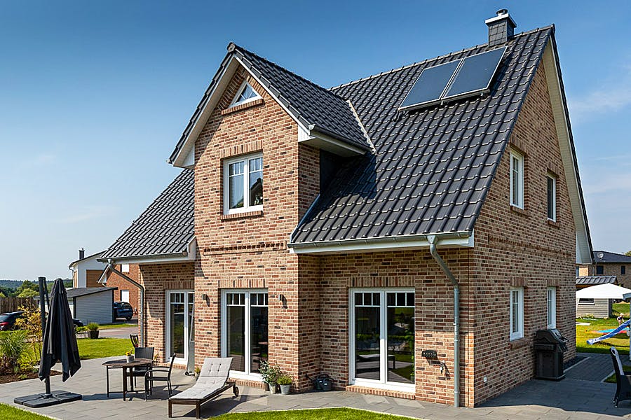 Julia und Martin aus Ahrensburg wollten raus aus der Mietwohnung. Ihr Zuhause sollte ein Neubau werden, weil die Bestandsimmobilien, die von Ihnen besichtigt wurden, zu viele Kompromisse bedeutet hätten. Wichtig war außerdem der Wunsch nach energiesparendem und nachhaltigem Bauen und ganz individueller Planung. 

„Eigentlich war ein Friesenhaus mit grünen Fenstern geplant, aber das Kapitänshaus unserer Kundenberaterin hatte uns dann noch besser gefallen.“ Der breite Kapitänsgiebel, zur Terrassenseite und nicht an der Vorderseite, schafft oben und unten einen architektonisch schönen Erker im Wohnbereich. So wurde ein Kapitänshaus mit 153 m² Wohnfläche, mit 3 Zimmern und einem Ankleidezimmer im Obergeschoss, einem Gäste-WC, Haustechnikraum sowie eines offenen Wohnbereiches im Erdgeschoss realisiert.