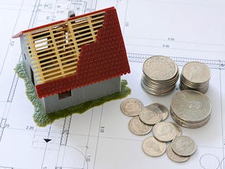 Hausmodell mit Münzen auf Bauplan