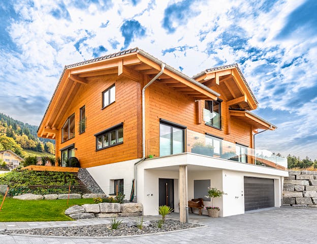 Modern interpretiertes Chalet in Blockbauweise mit charakteristischem Satteldach und weitem Dachüberstand, kombiniert mit einer hellen Putzfassade im Sockelbereich von Fullwood Wohnblockhaus. Statt traditioneller Schnitzereien prägen hier klare Linien, bodentiefe Fenster und eine transparente Glasbrüstung am Balkon den Stil – ein Chalet, das alpenländische Tradition mit zeitgemäßer Architektur verbindet.
