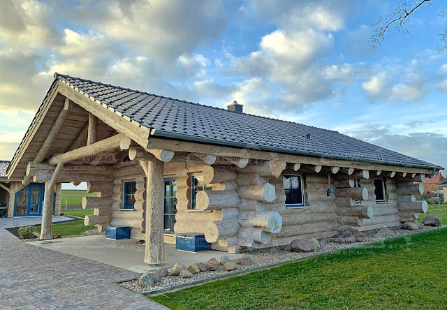 Ein Blockhaus von Holzbau Rustikal in Naturstammbauweise. Besonders eindrucksvoll sind die Säulen: Es sind Teile ganzer geschälter Bäume.