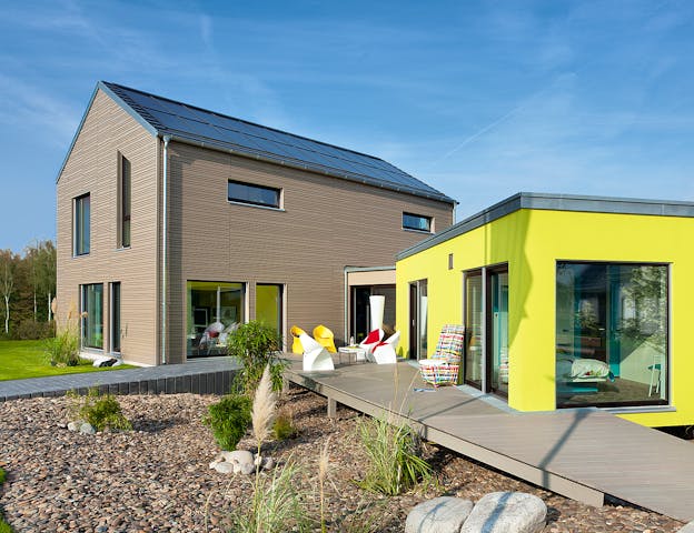 Modulhaus als Anbau an einem Satteldachhaus. Das Wohnmodul ist über einen Windfang mit dem Haupthaus verbunden und lässt sich als Büro oder Single-Apartment nutzen.